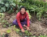 Woman smiling as she is sitting on the ground touching leaves. 