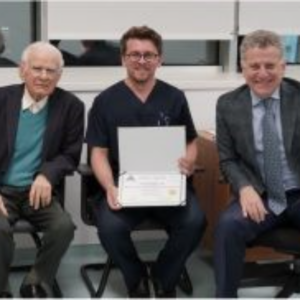 three men sitting with the man in the middle holding a certificate