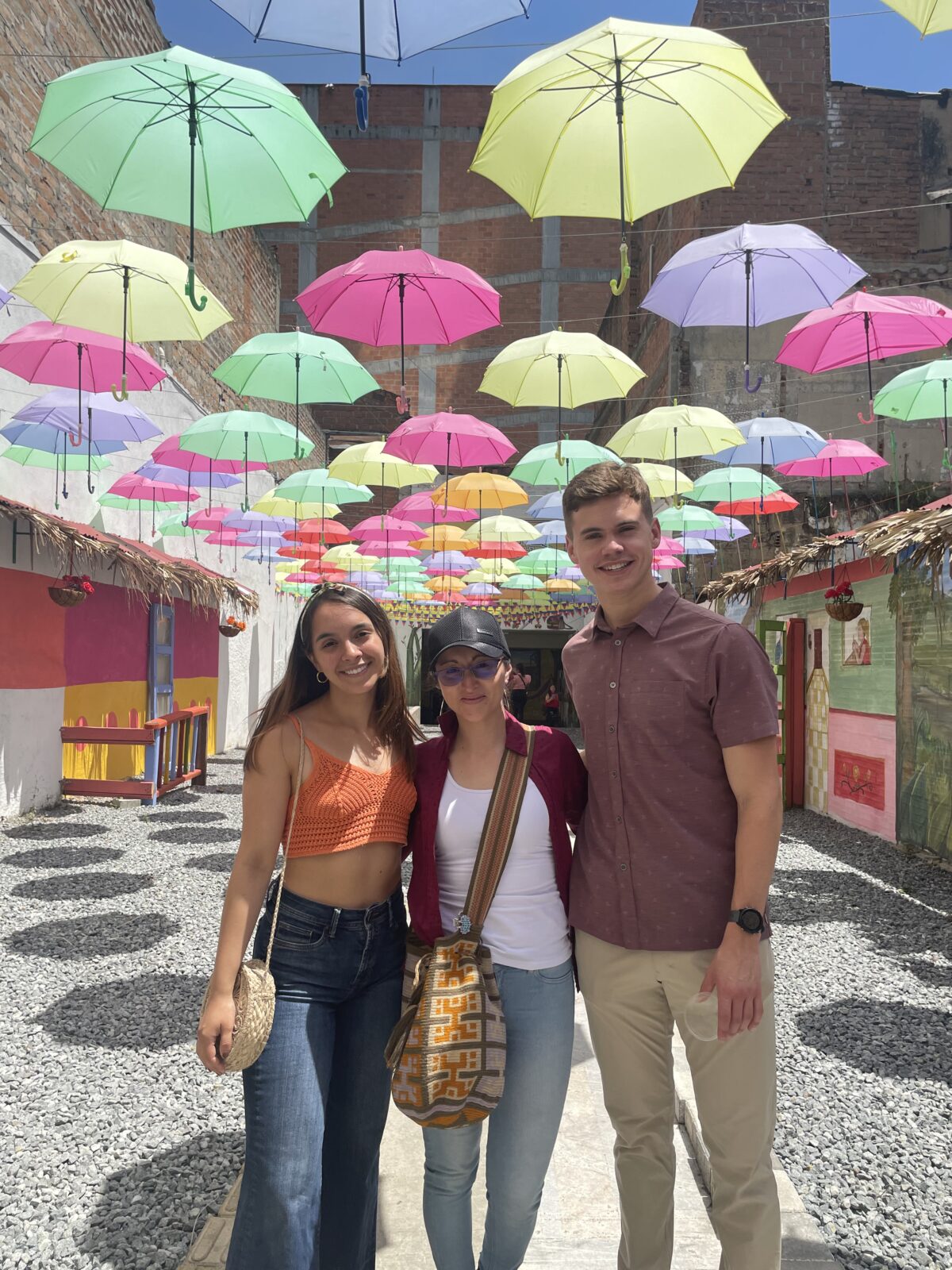 three people standing below colorful umbrellas on a gravel path