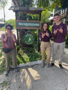 three poeple holding up and UW W with hands in front of a Colombian hotel