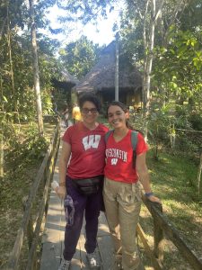 two women with dark hair wearing red UW Madison shirts in a forest area