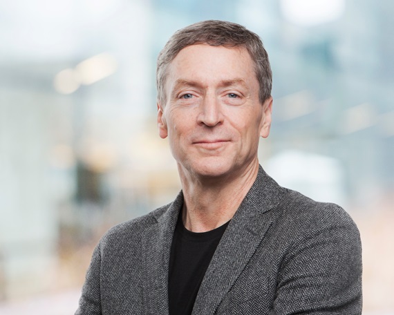 man with grey hair, grey suit and black shirt against a light indoor background
