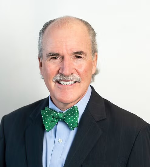 headshot of Peter Kilmarx, man with balding grey hair, dark jacket, blue shirt, green bow tie against a light background