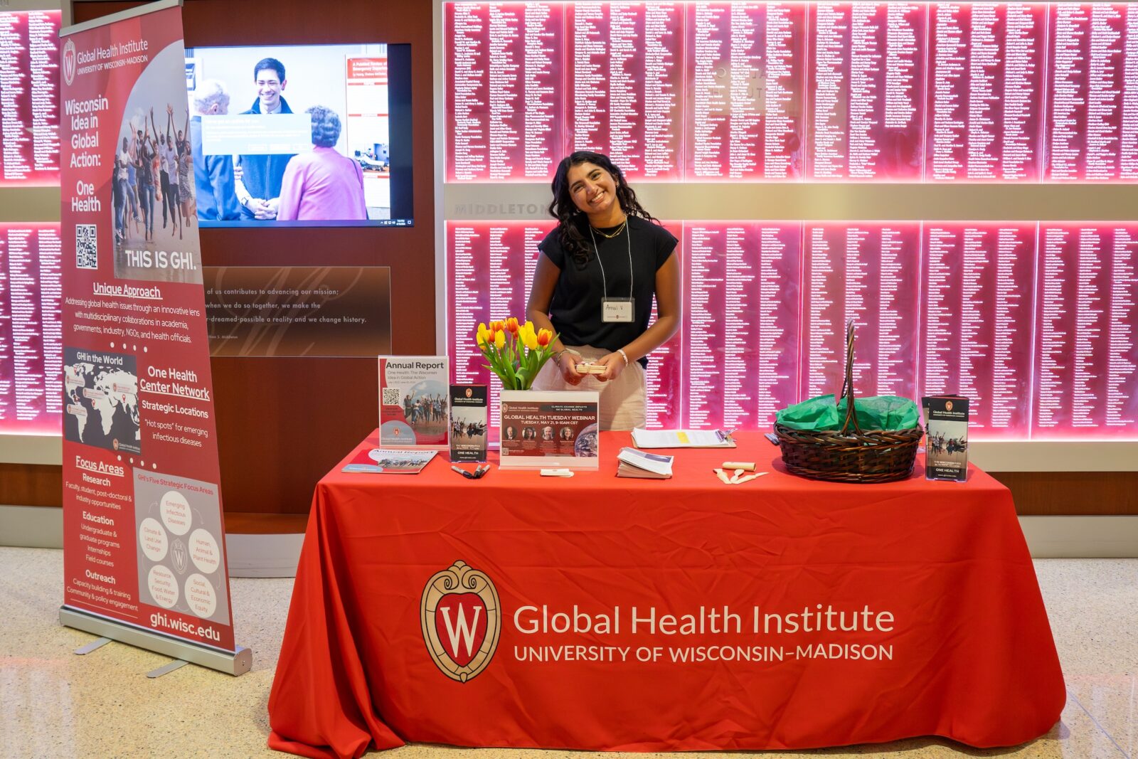 woman with dark hair at a table with a red tablecloth reading UW Global Health Institute against a red wall with list of words and a tv monitor on the left