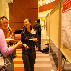 woman with glasses holding a plate discusses posters with two other women looking on