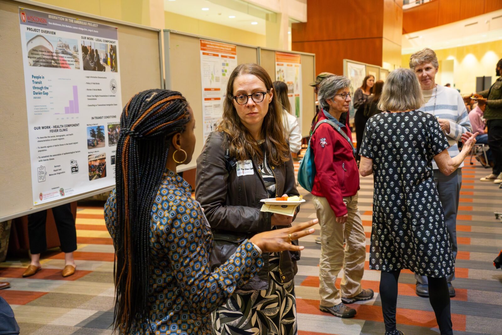 two women in discussion about a poster, woman on left has long dark hair in braids, woman on right has brown hair and glasses