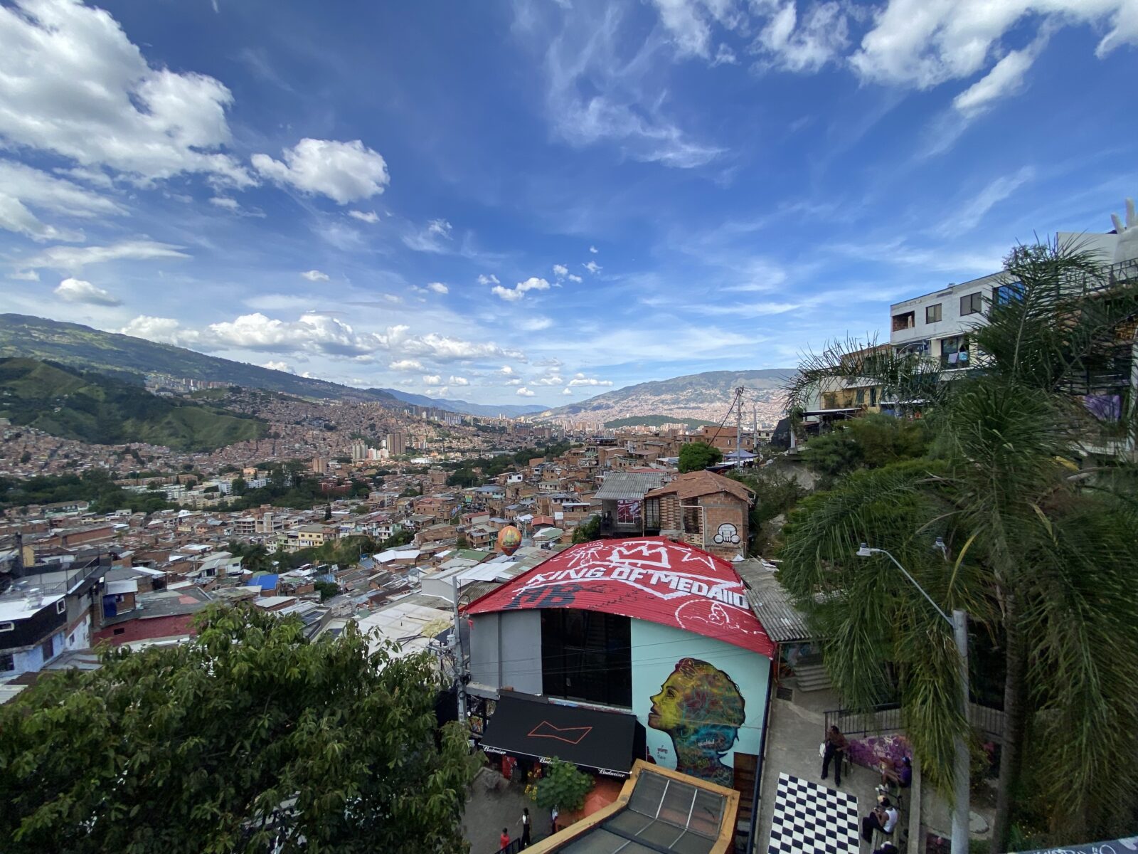 Scene at Comuna 13 with housing mural, housing, mountains, blue and white sky