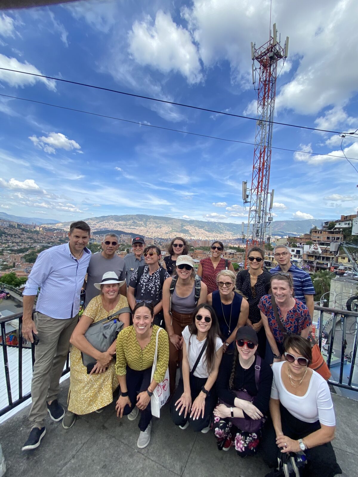 UW Madison Colombia delegation posing for a photo against the Comuna 13 backgroud, communication tower, housing, mountains, blue and white sky in background