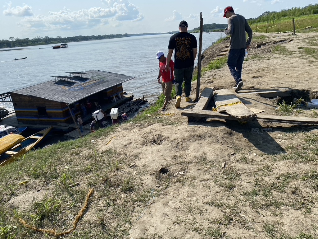 Approaching the boat launch to the Amazon river; three men walking on the hill, water and boathouse in the background, Sept 2023