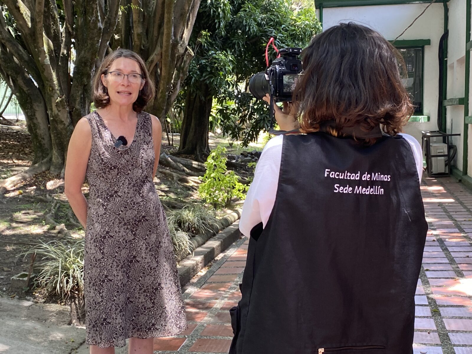 UW Madison Vice Provost and International Dean Frances Vavrus being interviewed at GHI OHC-Colombia, Sept 2023; woman standing in treed courtyard with another woman filming