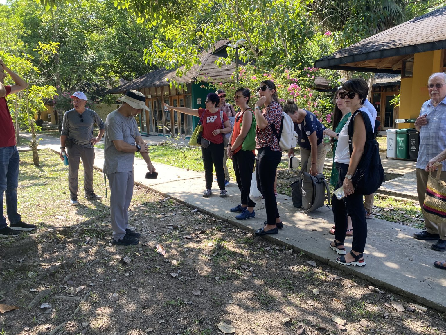UW Madison delegation hears UNAL Leticia campus information from Olga Lucia Chapparro, trees, buildings, people standing on walkway Sept 2023