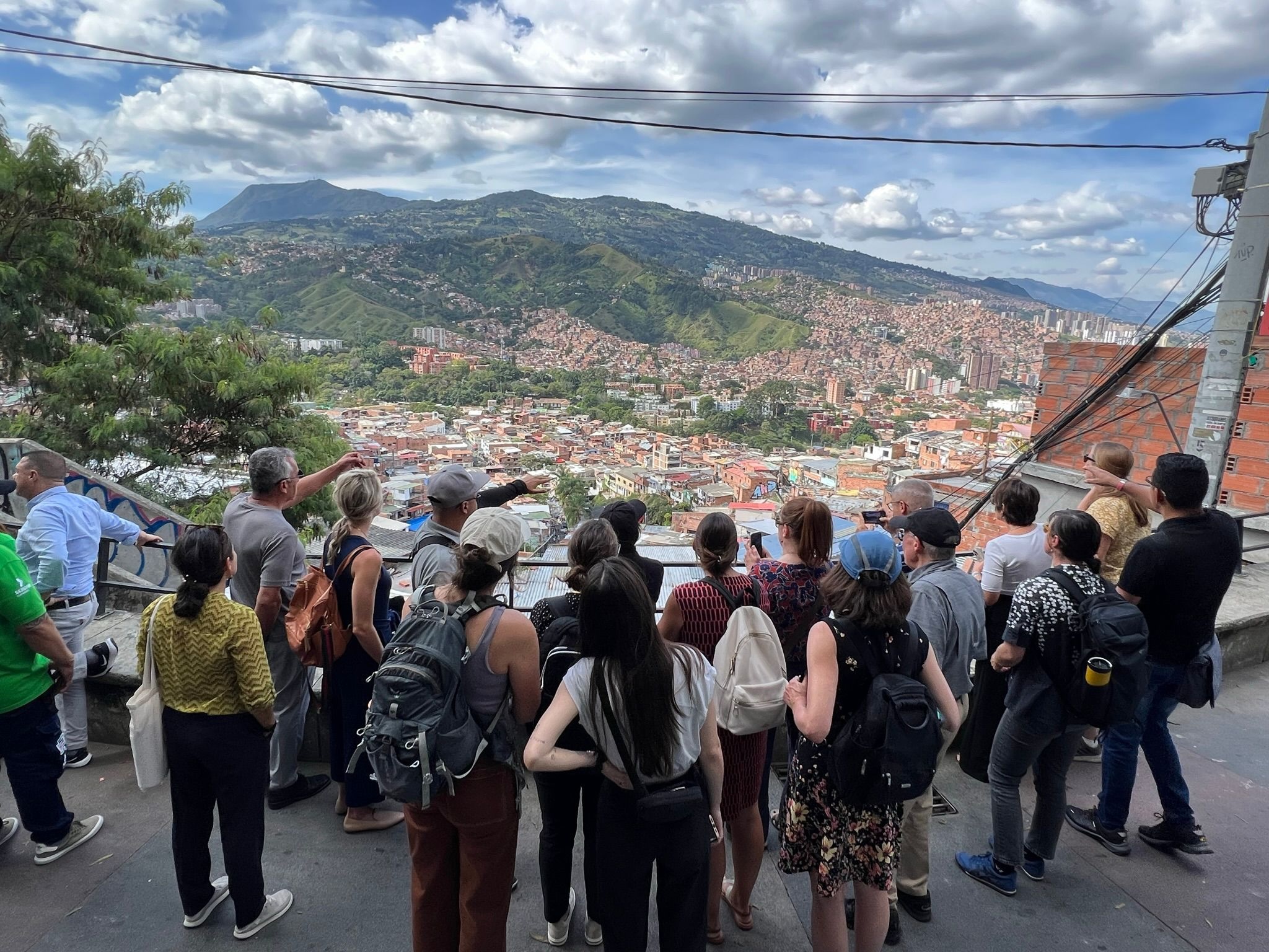 UW Madison delegation group overlooking Communa 13, Colombia; mountains, many housing units, electrical cables, cloudy sky