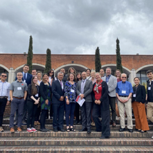 UW Madison Colombia delegation at Universidad Nacional de Colombia (Bogotá)standing on the steps to teh main campus brick building with four green trees in the background against a cloudy sky