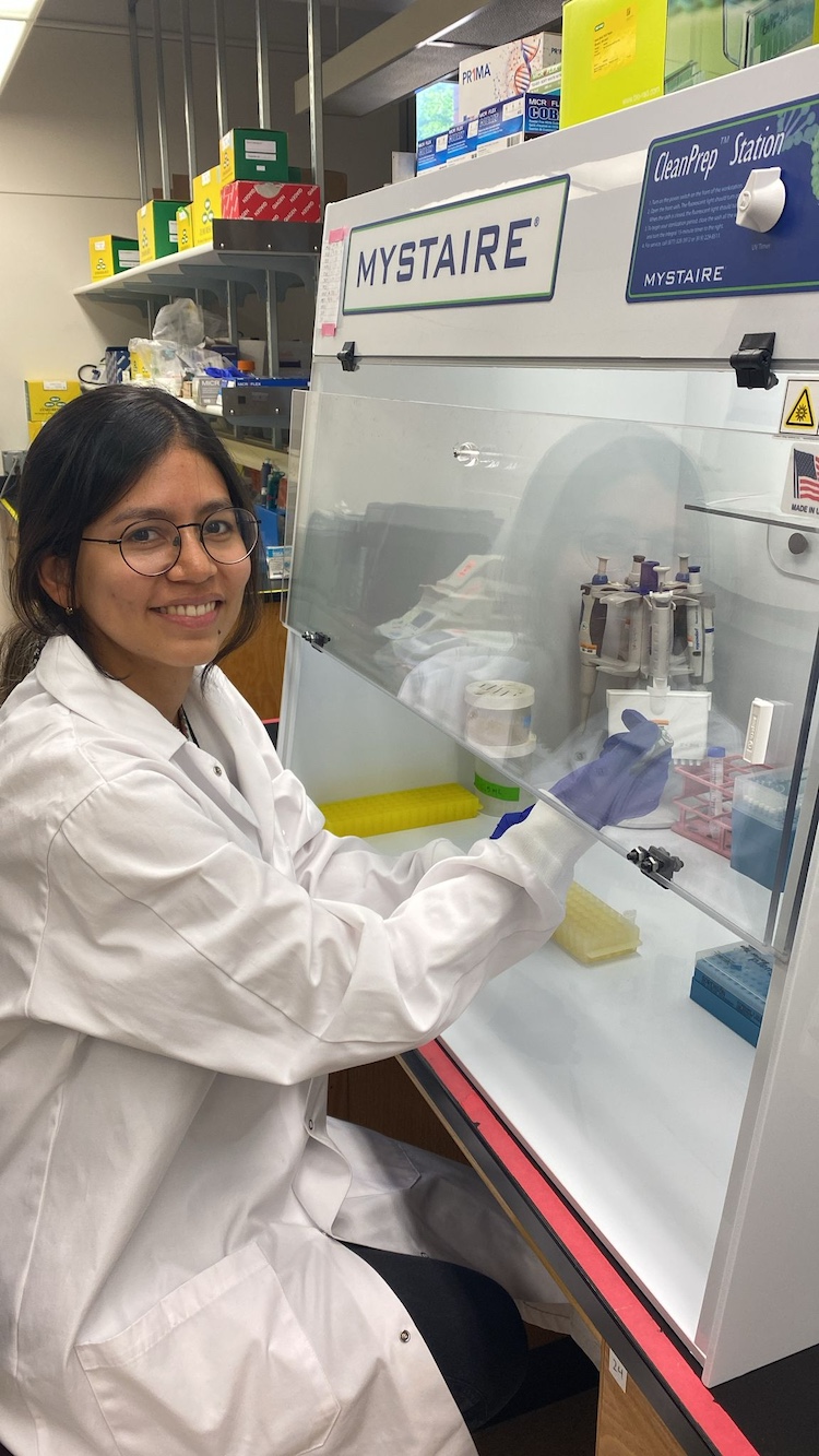 woman with dark hair and glasses in a white lab coat working in a lab setting