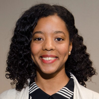 headshot of Nailah Smith, woman with dark hair, white jacket, black and white shirt against a grey background