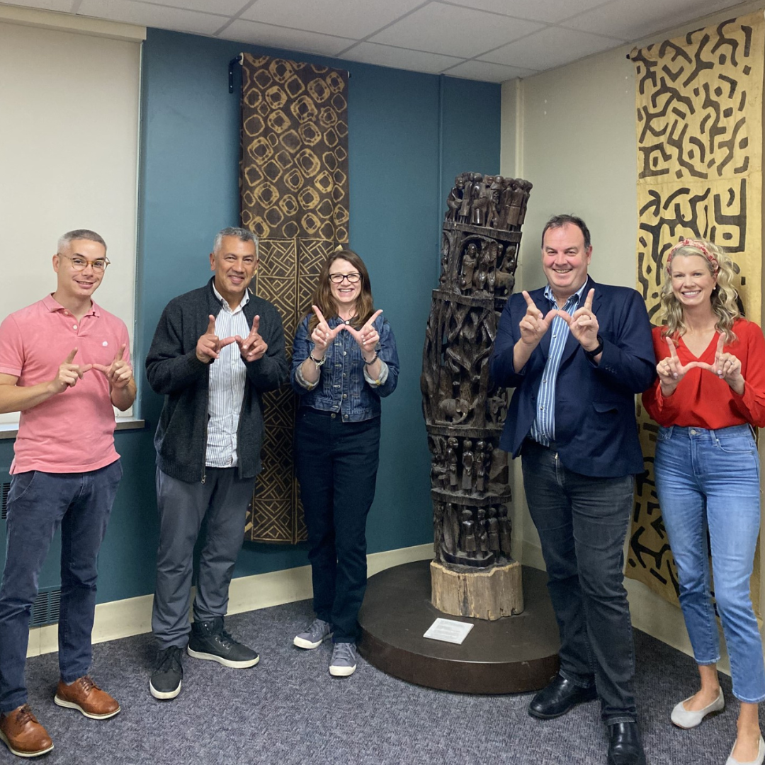 five people standing next to a dark wooden statue giving the UW W with their hands