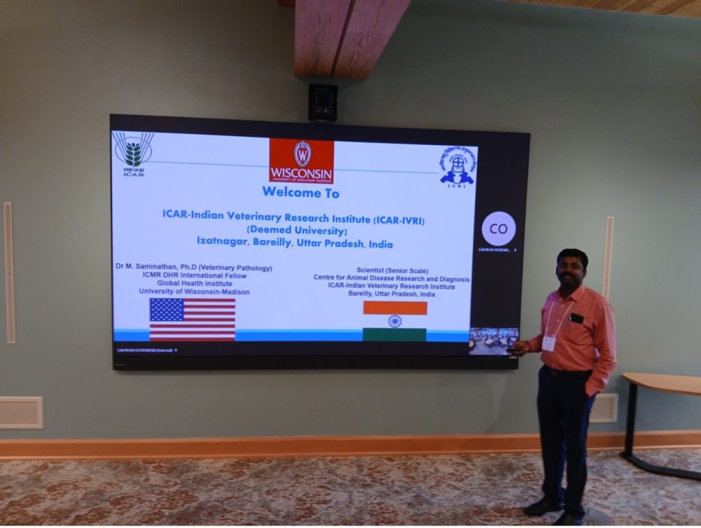 Photo S. Mani: Mani presenting his work at GHI's Advisory Committee Meeting/Retreat at Usona Institute in late July, man with dark hair and a red shirt standing next to a screen with a lide with text and the American and Indian flags