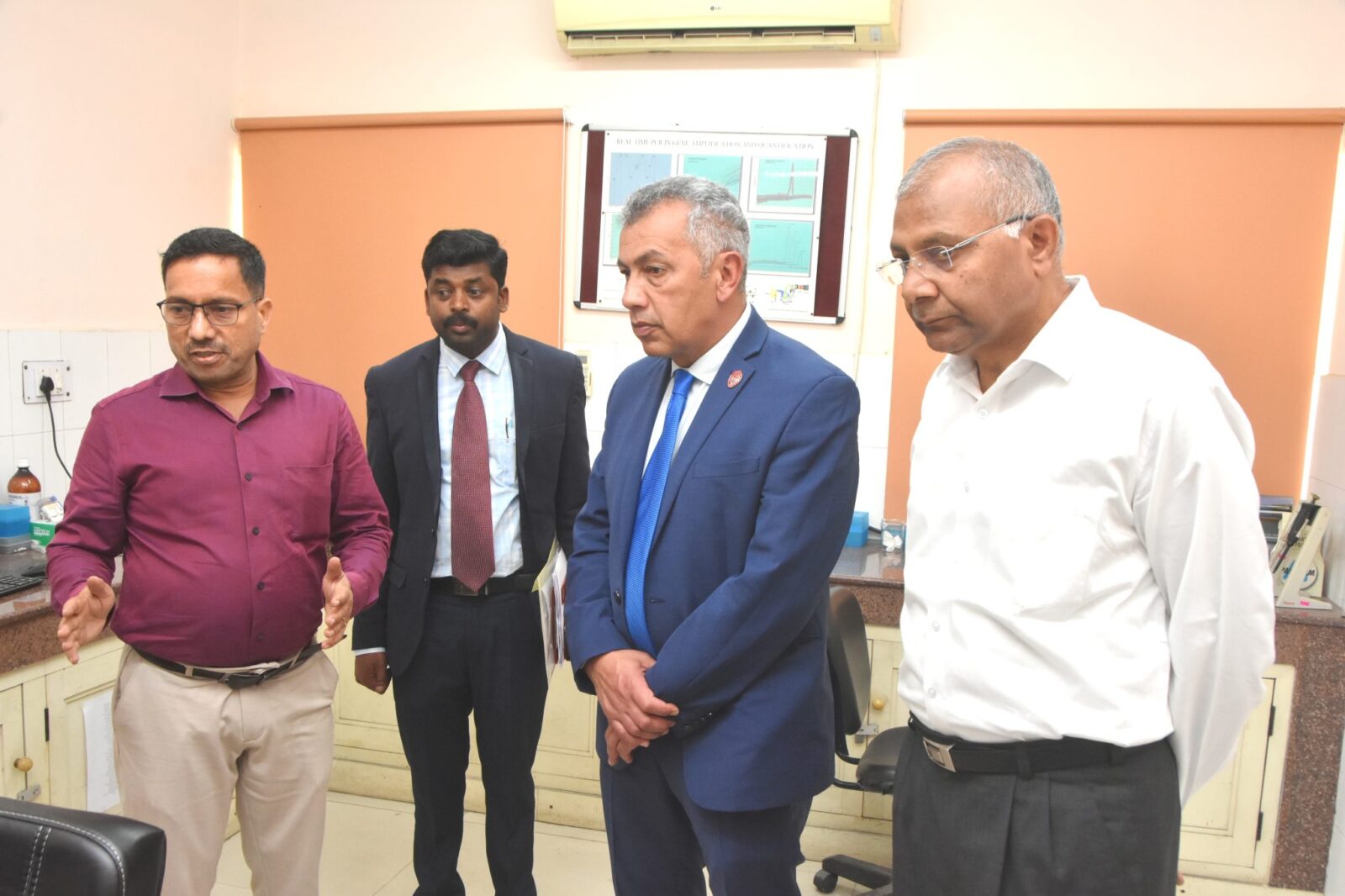Photo S. Mani: Saminathan Mani-second left with Jorge Osorio-second right, Triveni Dutt, Director, ICAR-IVRI-first right, and other scientists visiting various laboratories at ICAR-IVRI to explore ongoing research initiatives and technological advancement in veterinary sciences, four men standing and looking in the corner of the photo with an orange wall in the background