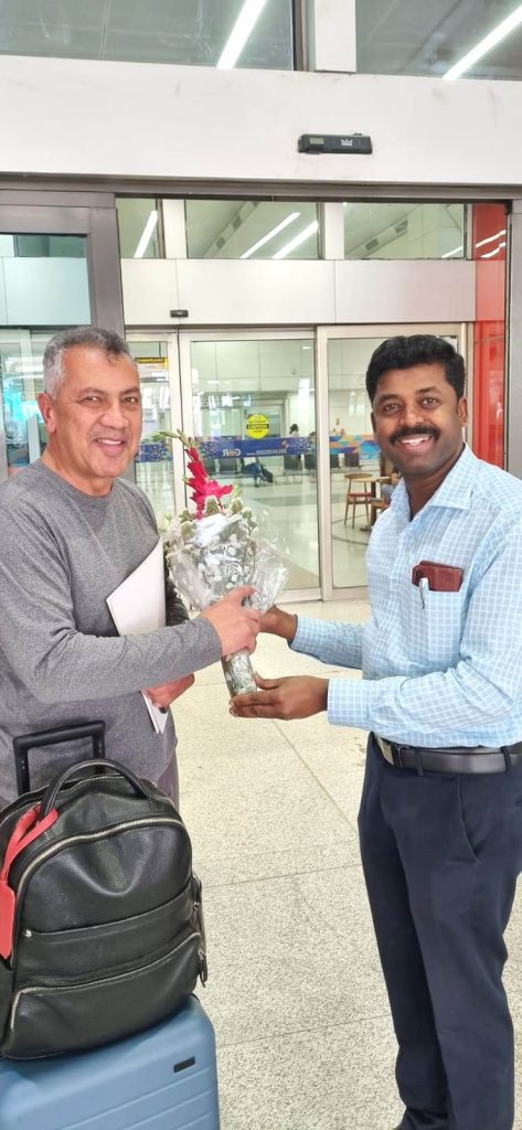 Photo S. Mani: Osorio-left, and Mani at IGI airport, Delhi, India, two men at an airport one giving flowers to the other