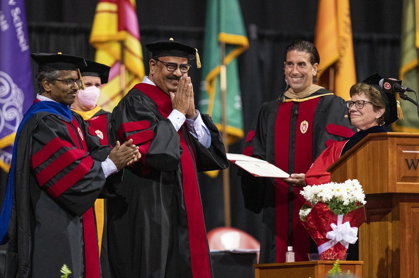 Dr. Ella wearing graduation garb standing on stage with four other people in graduation garb