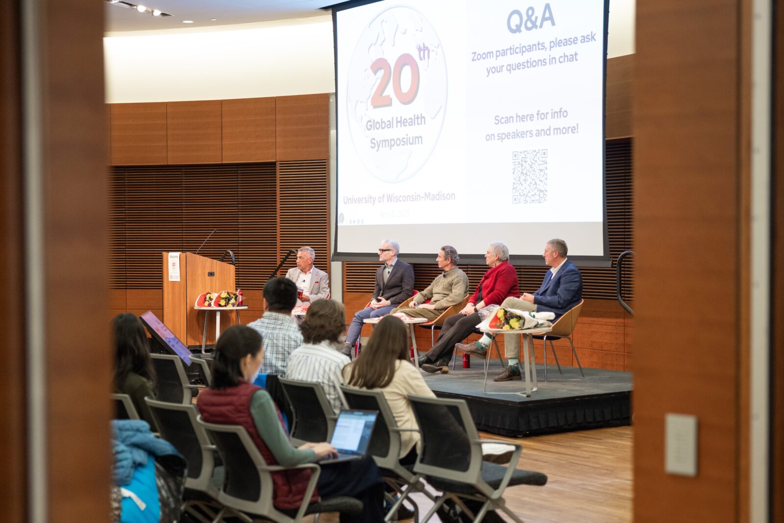 attendees sitting and watching a panel of five people sitting on a stage
