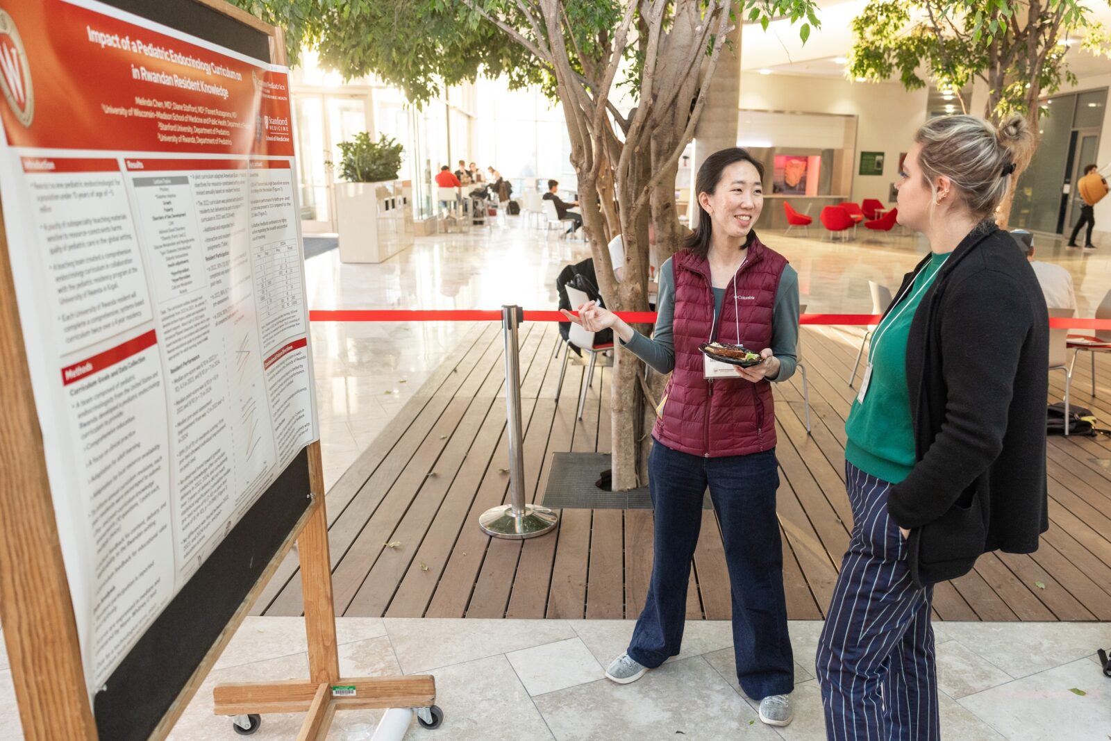 two women talking in front of a poster with a tree in the background