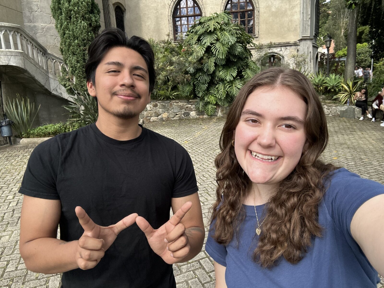 Justin and Kendall visiting Museo El Castillo (Photo courtesy K. Buehl) man in black shirt with dark hair holding up the UW W with hands and a woman with long dark hair in a courtyard
