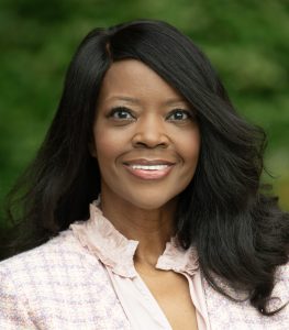 headshot of Jill Denson, woman with dark hair, pink shirt, against a green background