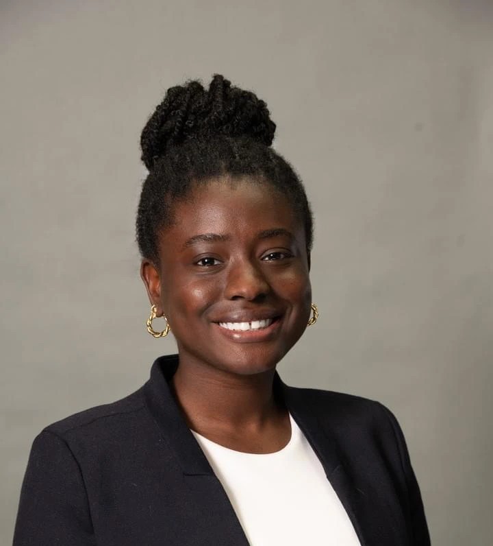 headshot of Tiwaladeolua Adekunle, woman with dark hair, dark jacket, white shirt against a grey background