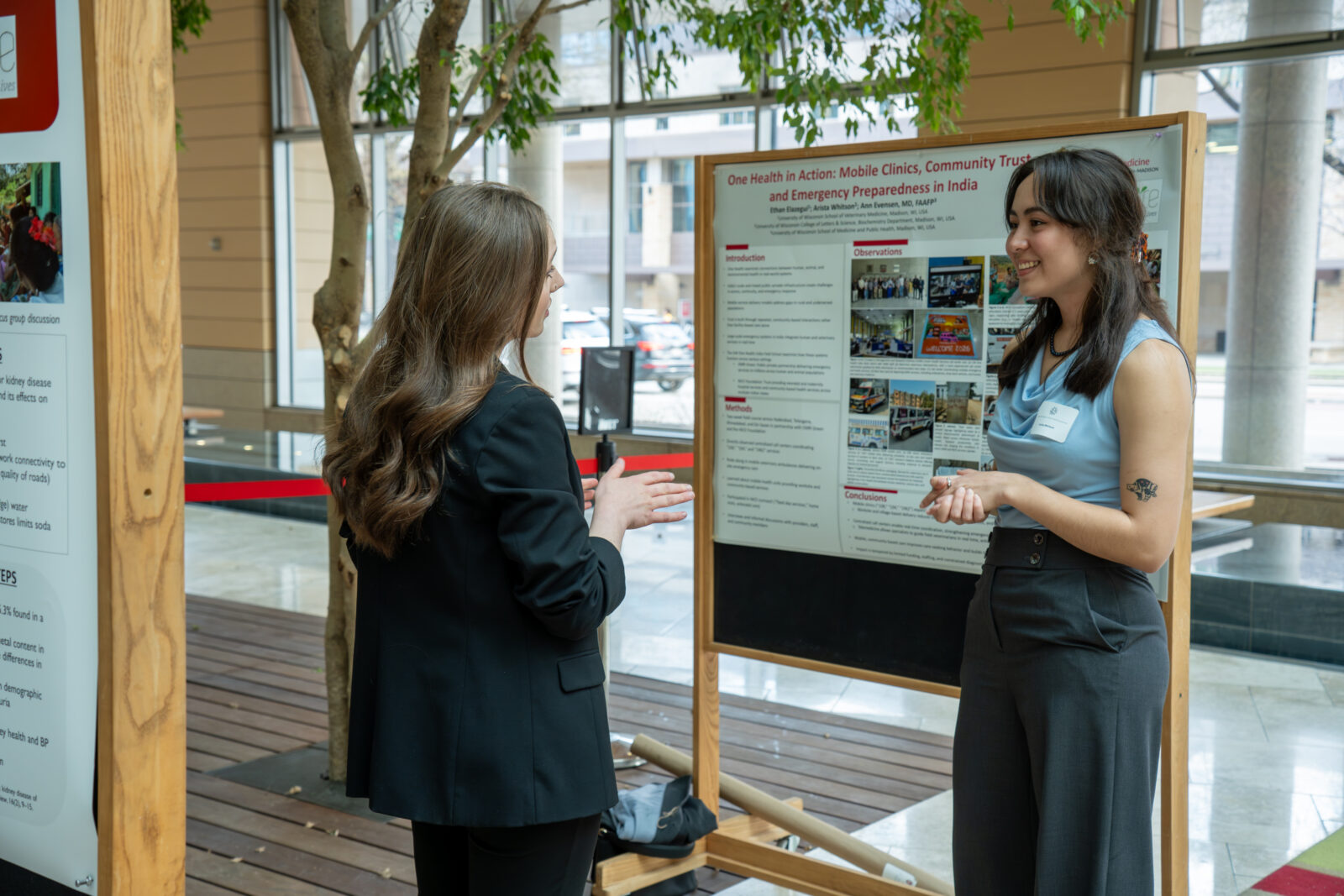 Photo from 2026 Global Health Symposium at the Discovery Building; two women standing in front of a poster in the discovery building atrium
