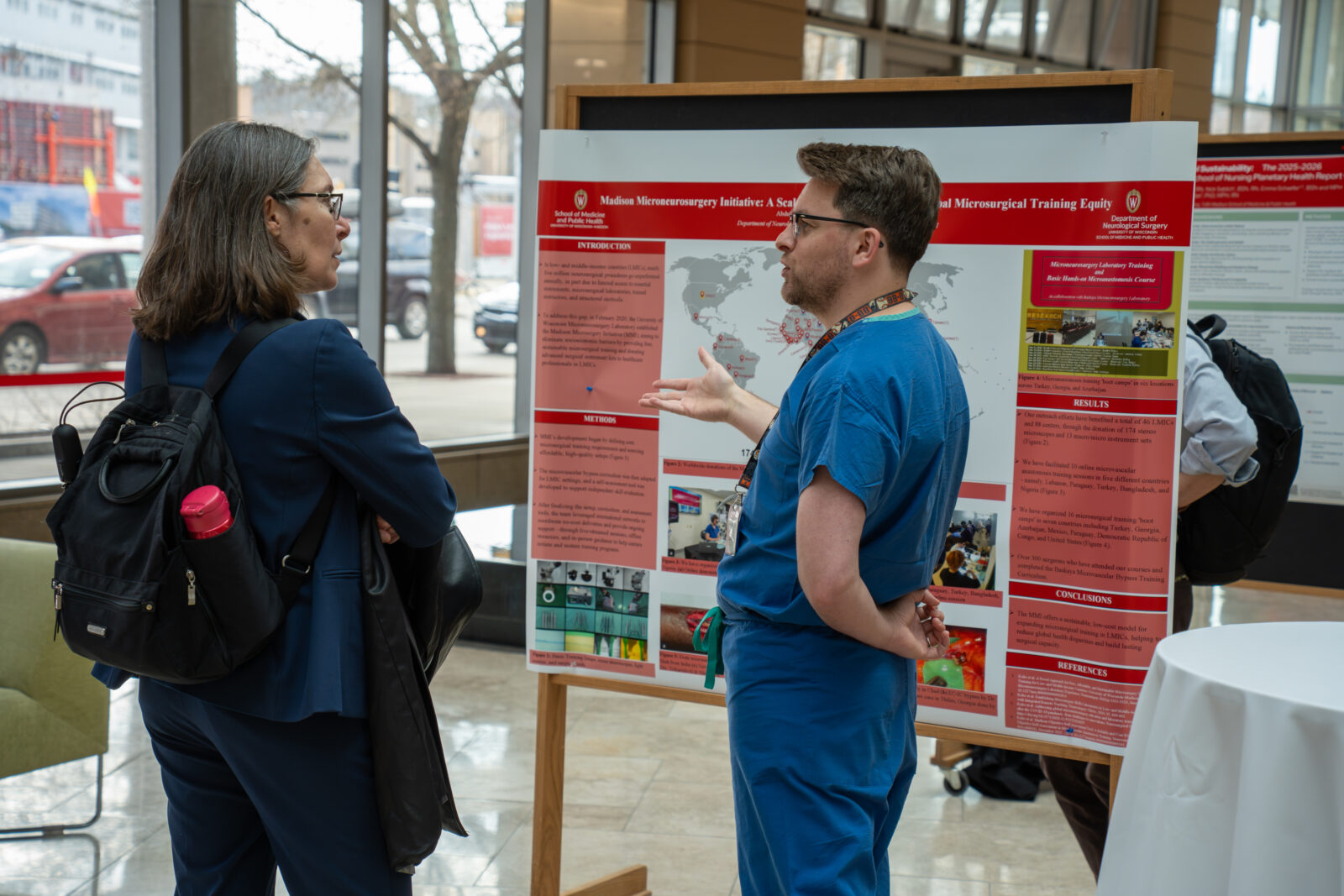 Photo from 2026 Global Health Symposium at the Discovery Building; Dr Vavrus with Abdullah Keles in a blue scrubs shirt in front of a poster