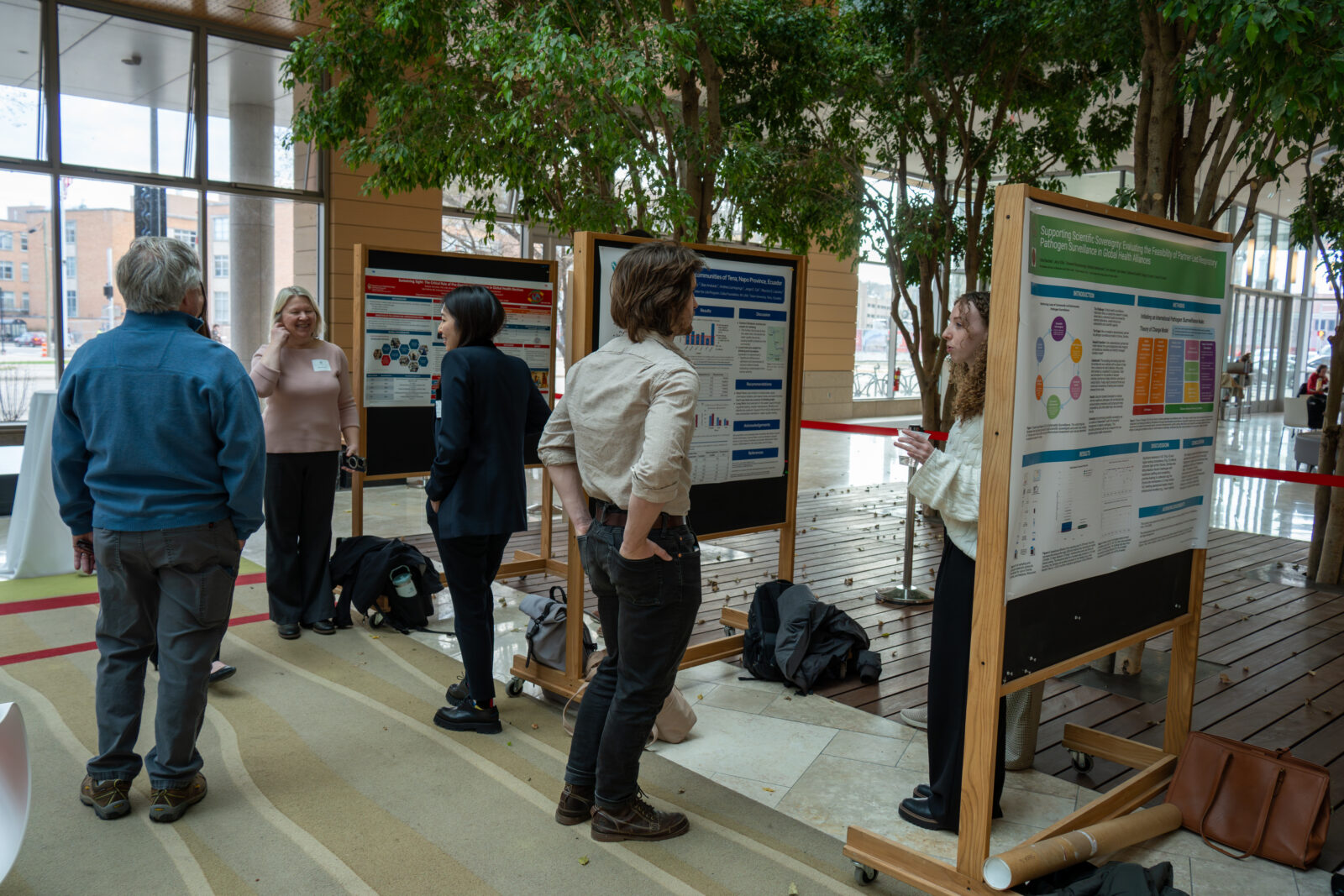 Photo from 2026 Global Health Symposium at the Discovery Building; people looking at posters in the atrium, trees and windows also in the photo