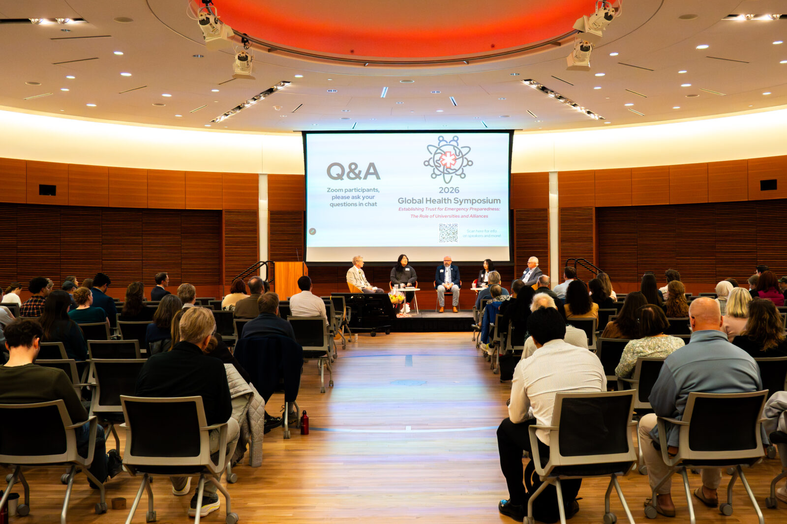 Photo from 2026 Global Health Symposium at the Discovery Building; full shot of panel from back of room with a Q&A slide on the screen and showing people sitting in chairs