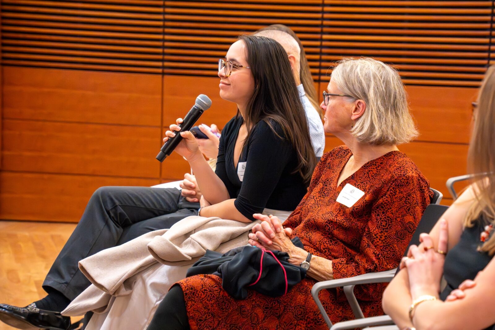 Photo from 2026 Global Health Symposium at the Discovery Building; student in a black shirt sitting with a microphone asking a question while other look on