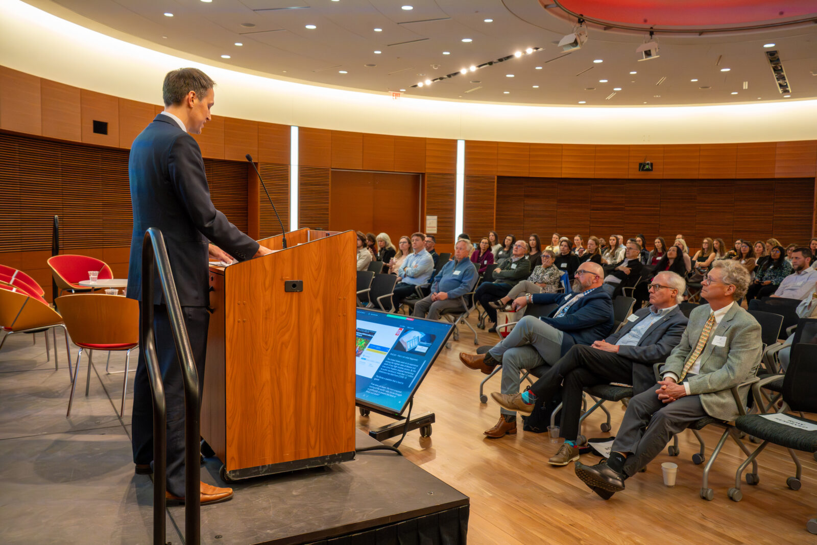 Photo from 2026 Global Health Symposium at the Discovery Building; Dr. Westergaard at lectern with front row attendees sitting