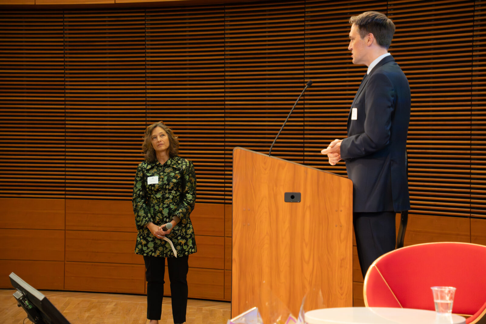 Photo from 2026 Global Health Symposium at the Discovery Building; Dr. Ryan Westergaard at the lectern with Dr. Jennifer Kushner standing below with a green decorative jacket