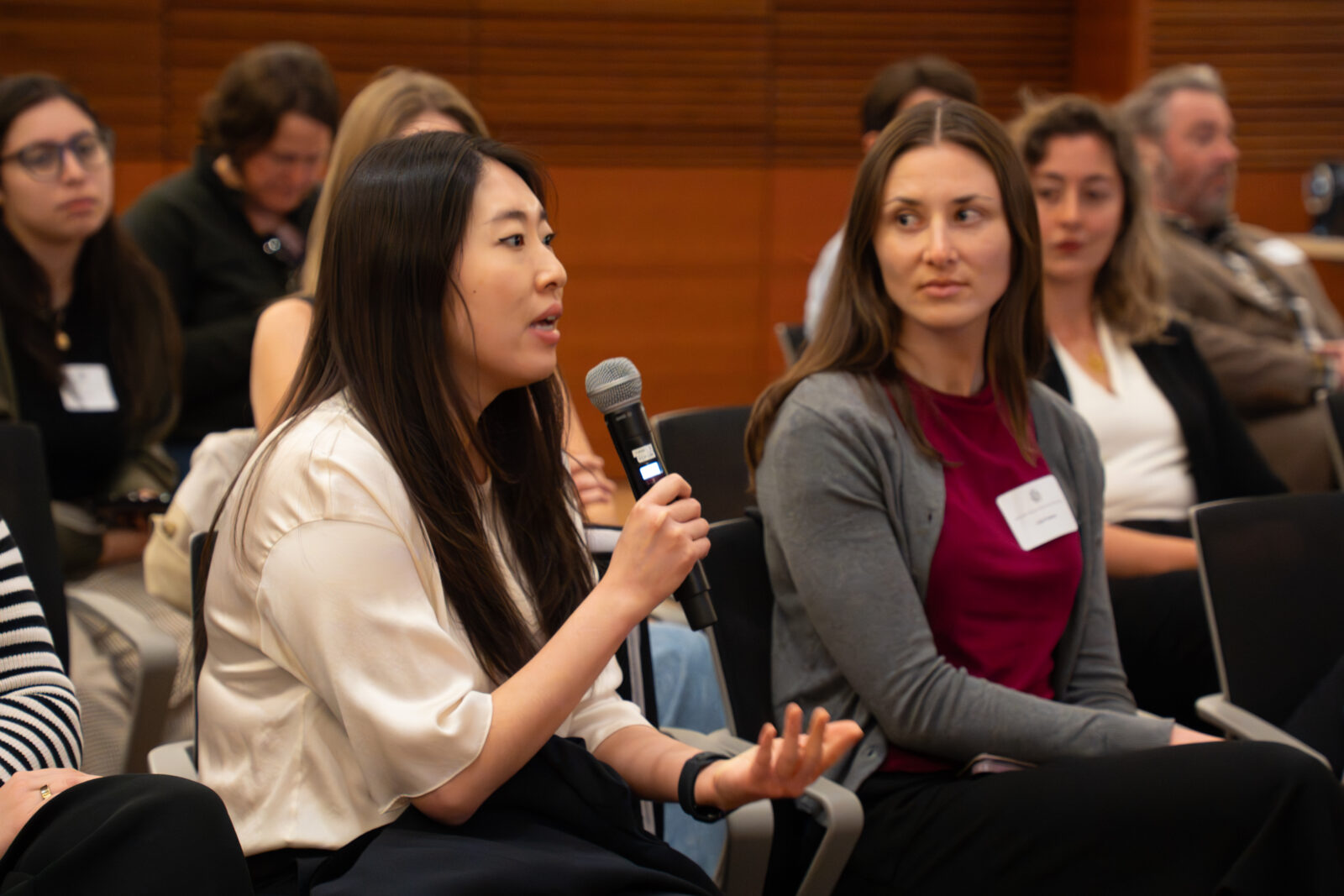 Photo from 2026 Global Health Symposium at the Discovery Building; Woman with dark hair and light top sitting with mic asking a question while others look on