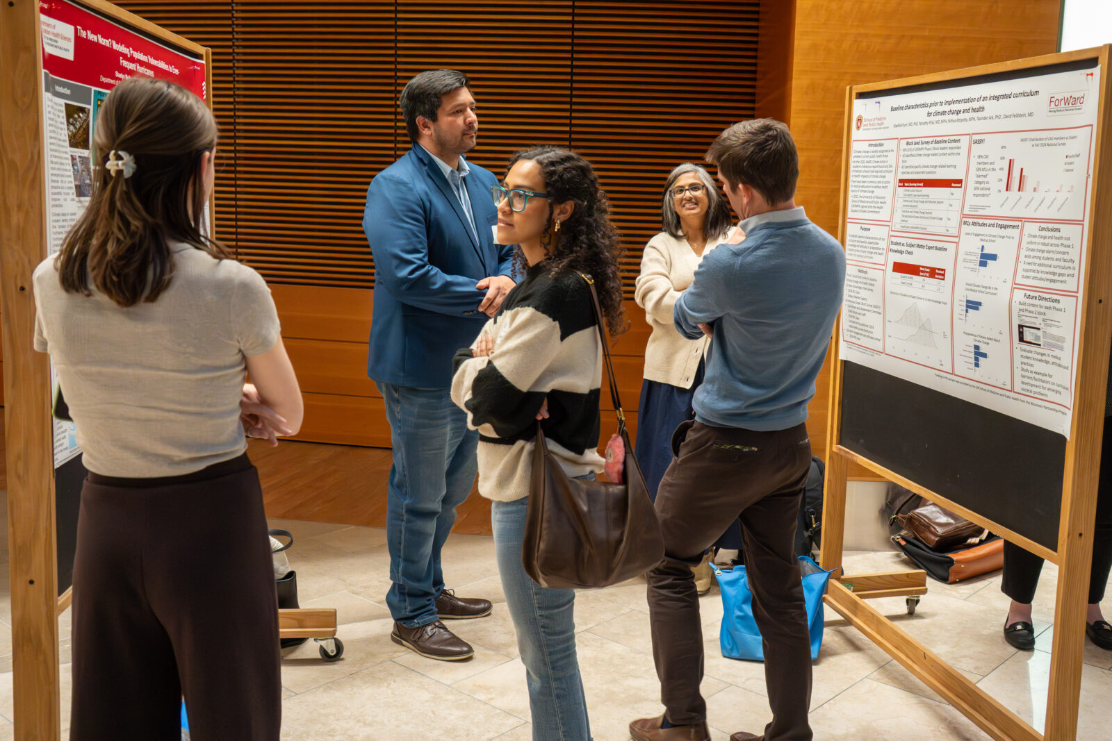 Photo from 2026 Global Health Symposium at the Discovery Building; students looking at a poster board in the discovery building atrium