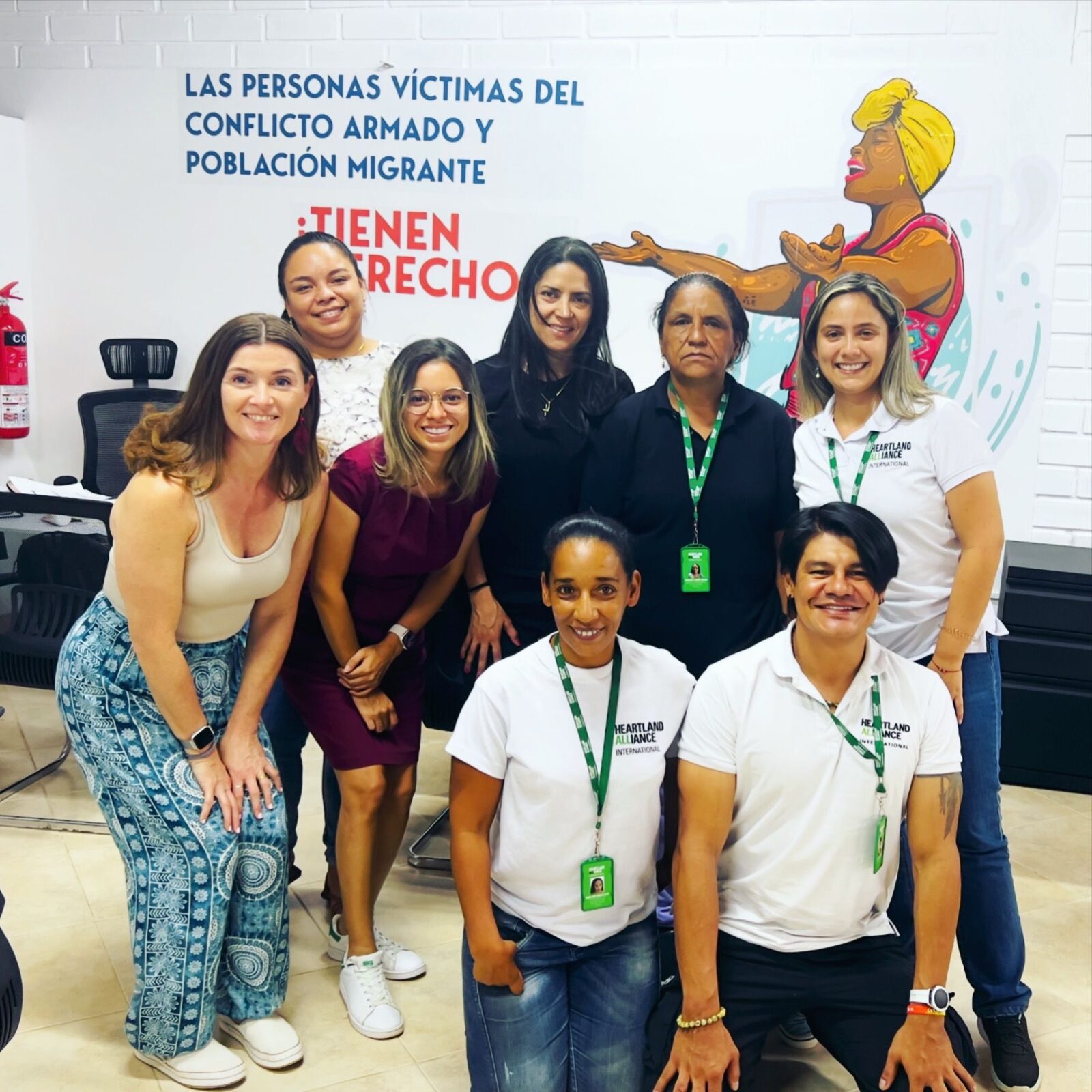 May 2024, group of peole standing and kneeling with a mural and words on the wall in the background