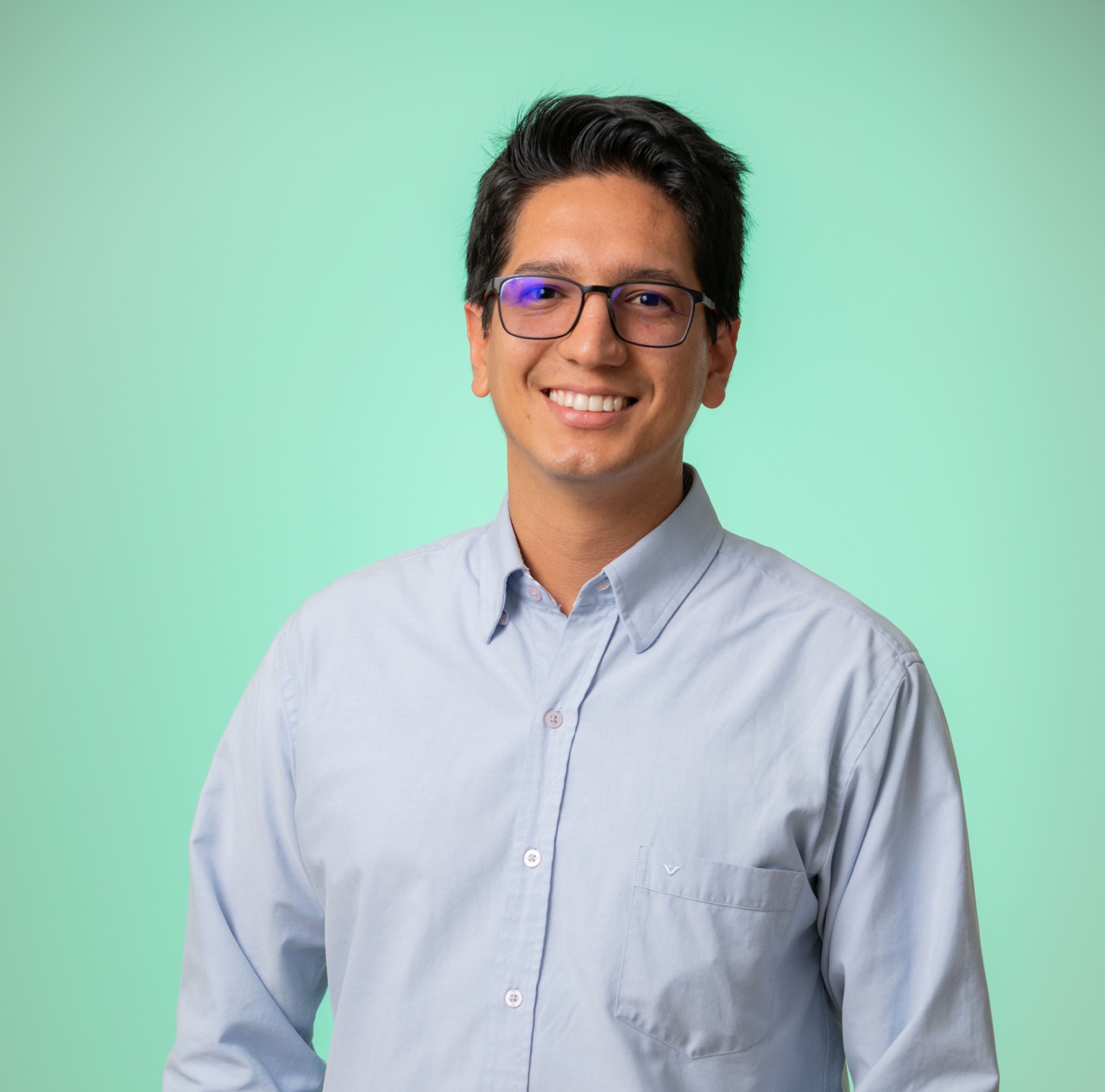 August 2024, man with dark hair and glasses, blue shirt against a green background