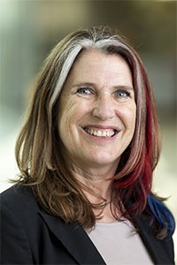 Dominique Brossard March 2024, woman with multicolored hair in a dark top against an outdoor background