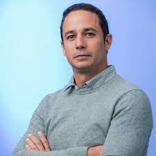 October 2023 Colombia article, man with dark hair, grey sweater & shirt against a blue and purple background