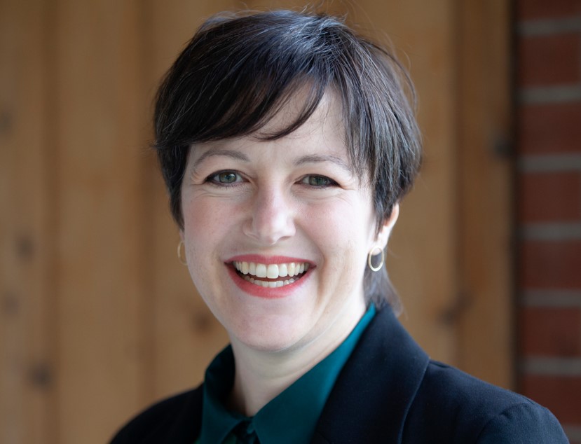 November 2024, woman with dark hair, dark jacket and shirt against a wood background