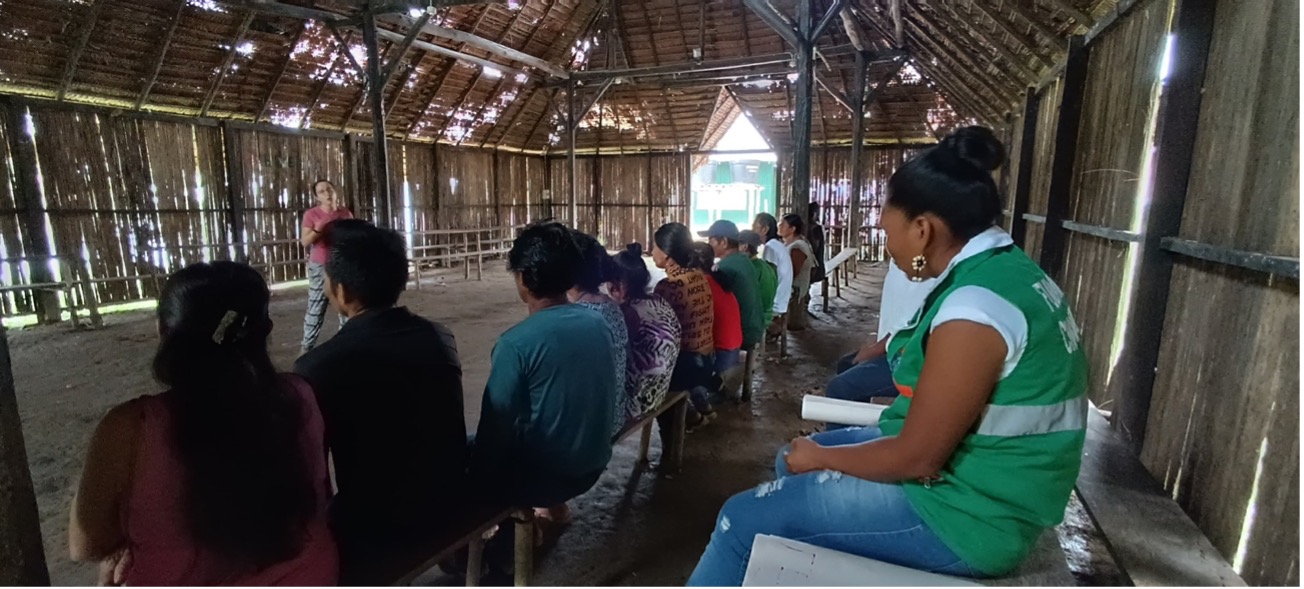 June 2024, inside a malorca, thatched building with open doorway, people sitting listening to one woman