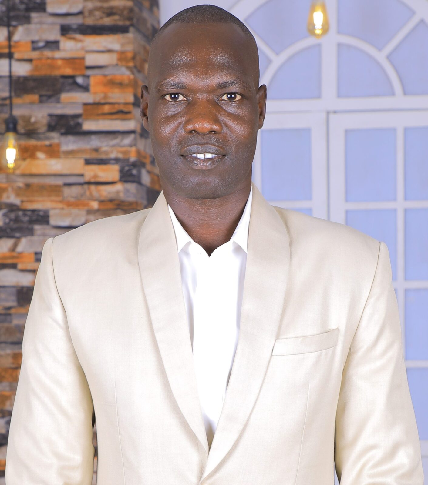 November 2023 Global Health Tuesday: Energy Challenges man with dark hair, white suit against a background with a stone wall and white window
