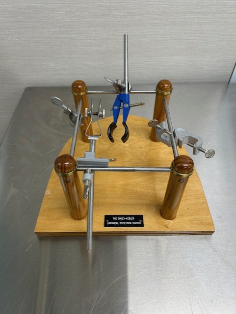 photo of the first laryngeal station; plywood, steel rods, brass rings, test tube clamps with small plaque on a clear table