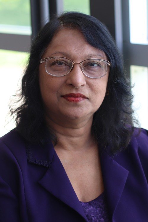 July 2023, woman with dark hair, glasses, purple top against a window background