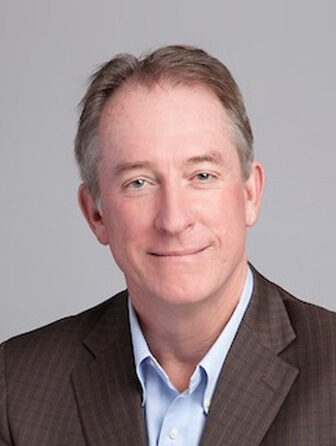 January 2024, man with grey hair, dark jacket, light shirt against a light grey background