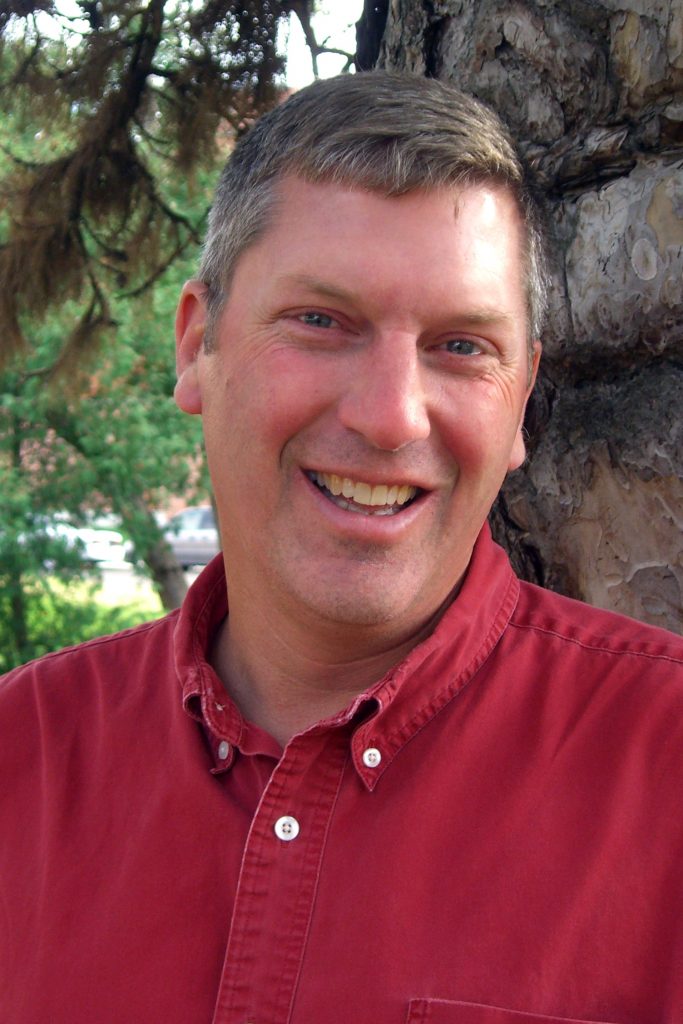 February 2025, man with dark grey hair and a red shirt in front of a tree