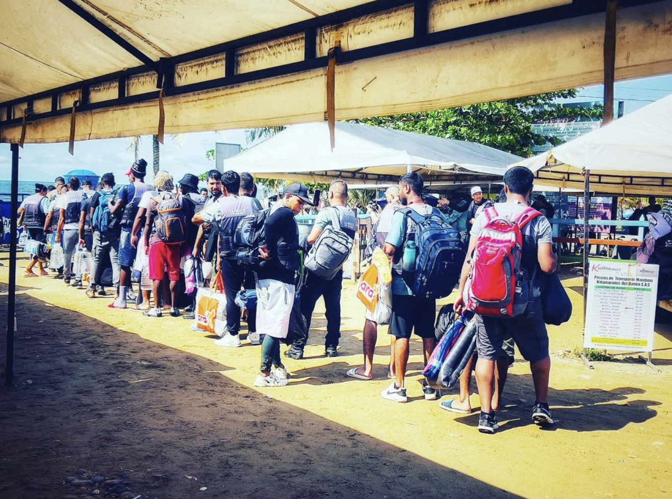 March 2024, a line of people waiting in a line with bags under a tent with a yellow floor